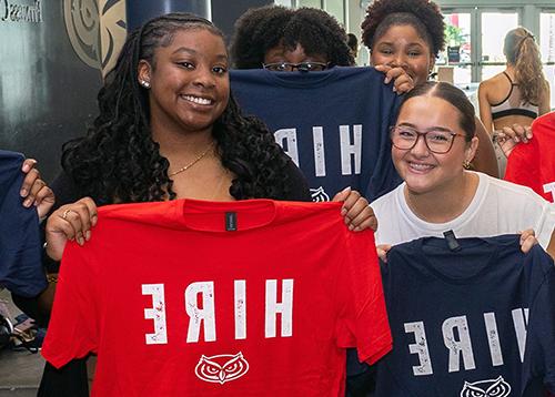 A student holding up a red shirt that says HIRE